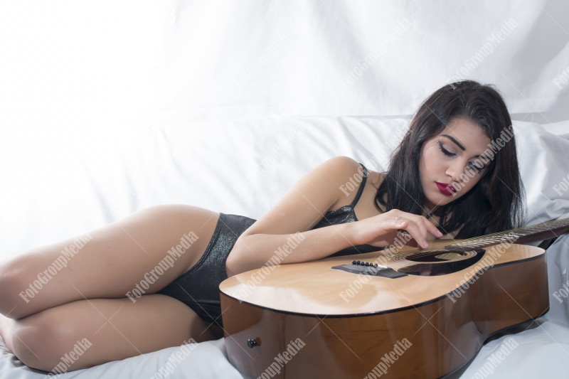 Brunette young girl and guitar posing on bed