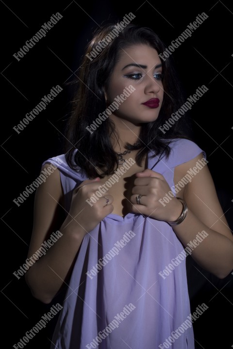 Fashion model posing in studio wearing purple dress on black background