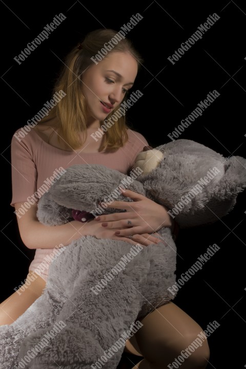 Young beautiful girl hugging big huge teddy bear soft toy on black background.