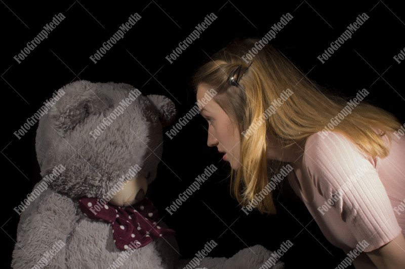 Young woman sharing secrets with her big huge teddy bear at tea time.