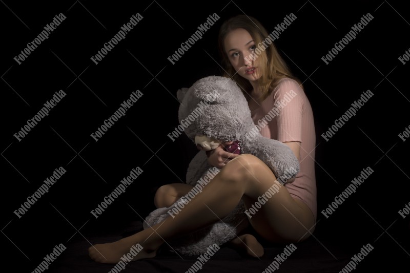 Young beautiful girl hugging big huge teddy bear soft toy on black background.