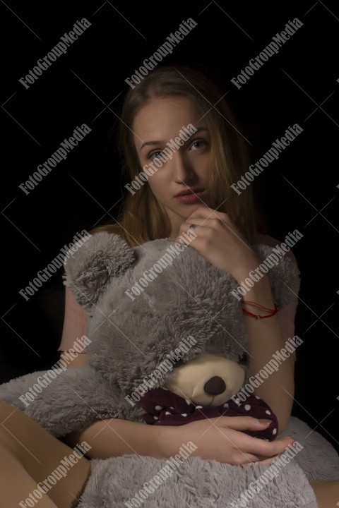 Young beautiful girl hugging big huge teddy bear soft toy on black background.