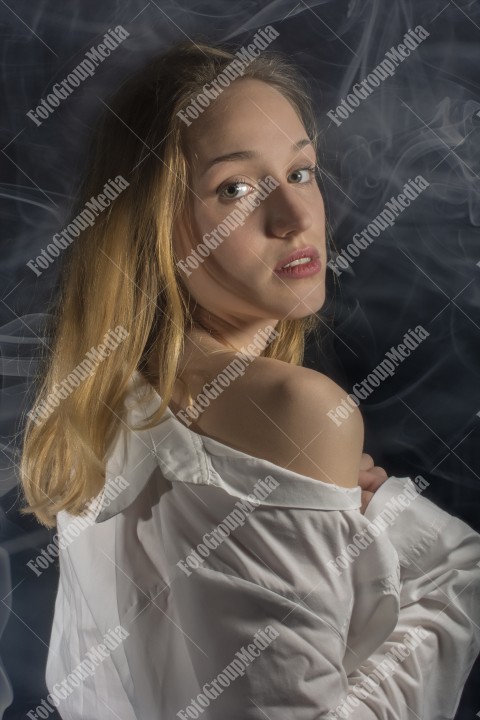 Fashion model posing in studio wearing white shirt on smokey background