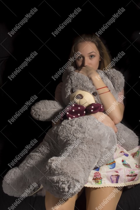 Young woman hugging her big teddy on black background