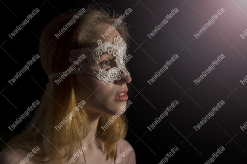 Portrait of a shy girl wearing lace mask on black background