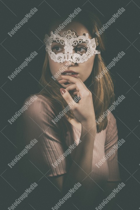 Portrait of a shy girl wearing lace mask on black background