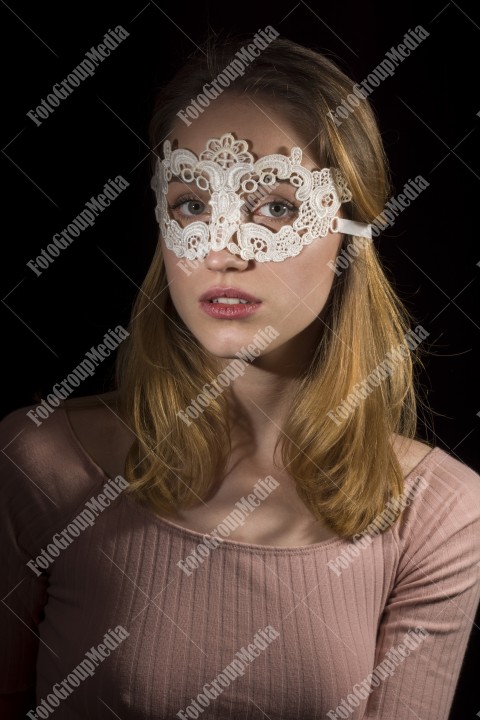 Portrait of a shy girl wearing lace mask on black background