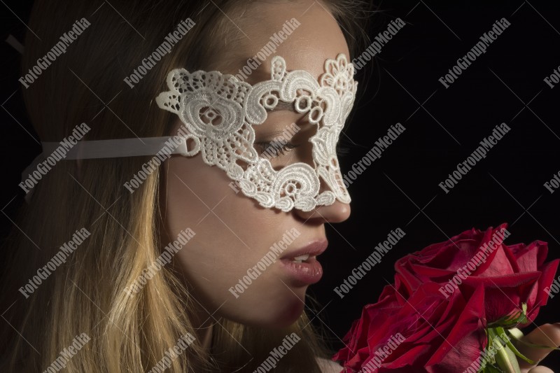 Close up portrait of a shy woman wearing mask and red roses on black background