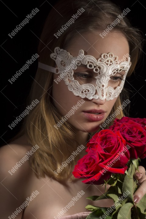 Close-up portrait mysterious attractive woman. Black background, with lace mask on face, red roses.