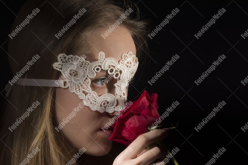 Close up portrait of a shy woman wearing mask and red roses on black background