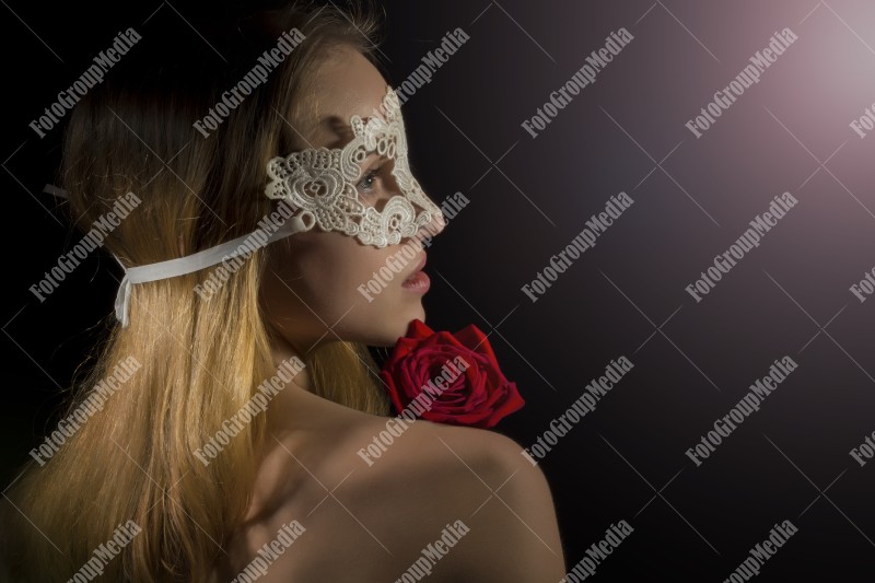 Close up portrait of a shy woman wearing mask and red roses on black background