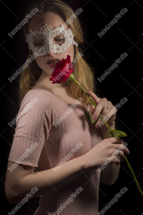 Portrait of a shy girl wearing mask and red rose on black background