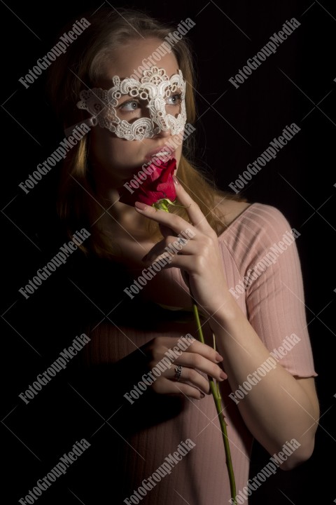 Portrait of a shy girl wearing lace mask and red rose on black background