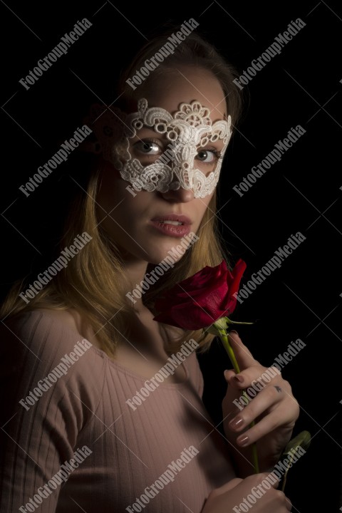 Portrait of a shy girl wearing lace mask and red rose on black background