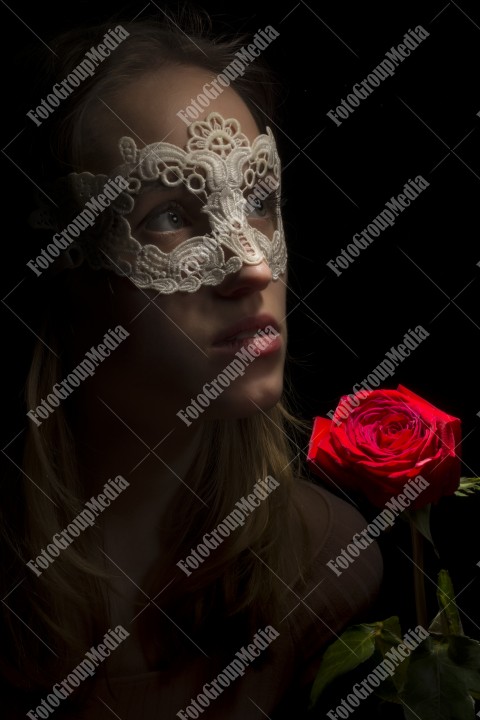 Portrait of a shy girl wearing lace mask and red rose on black background