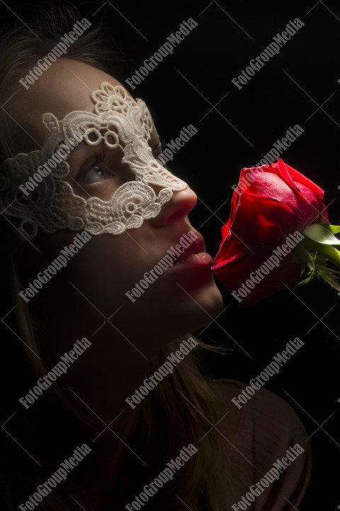 Close up portrait of a shy woman wearing mask and red roses on black background