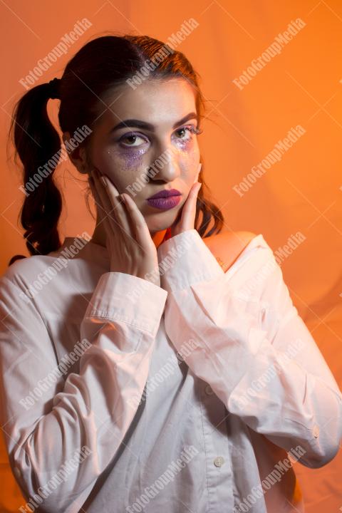 Young girl with two pony tails and artistic make up on yellow background