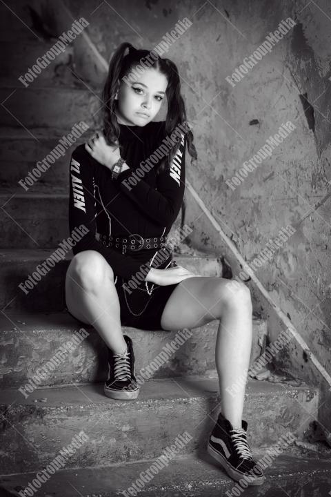 Young woman posing in a tight gym bodysuit sitting on broken stairs