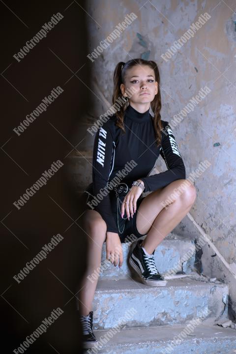 Young woman posing in a tight gym bodysuit sitting on broken stairs
