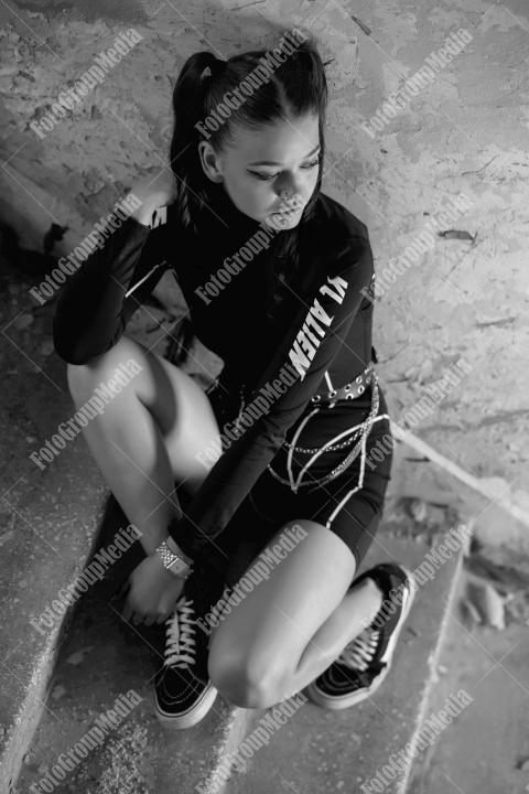 Young woman posing in a tight gym bodysuit sitting on broken stairs
