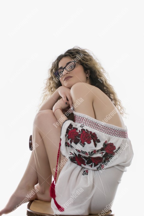Woman with curly hair and white dress with red flowers posing on white background