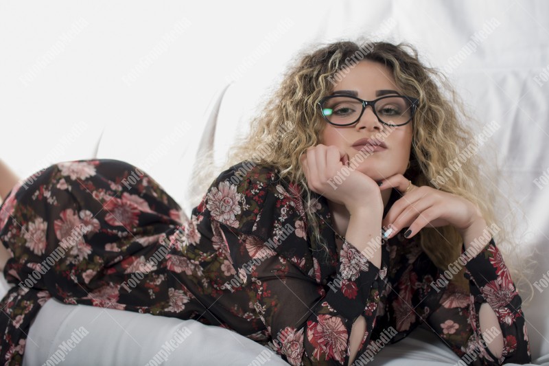 Woman with curly hair and floral dress posing on bed