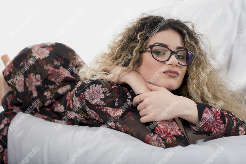 Woman with curly hair and floral dress posing on bed