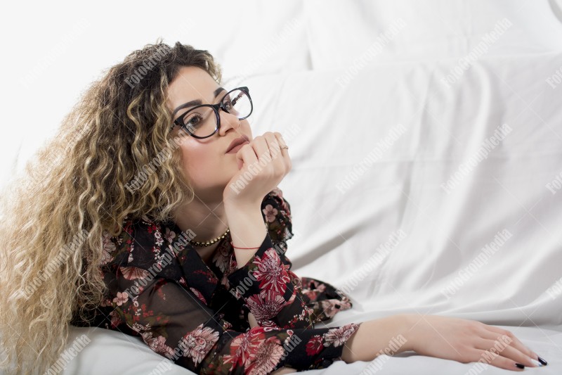 Woman with curly hair and floral dress posing on bed