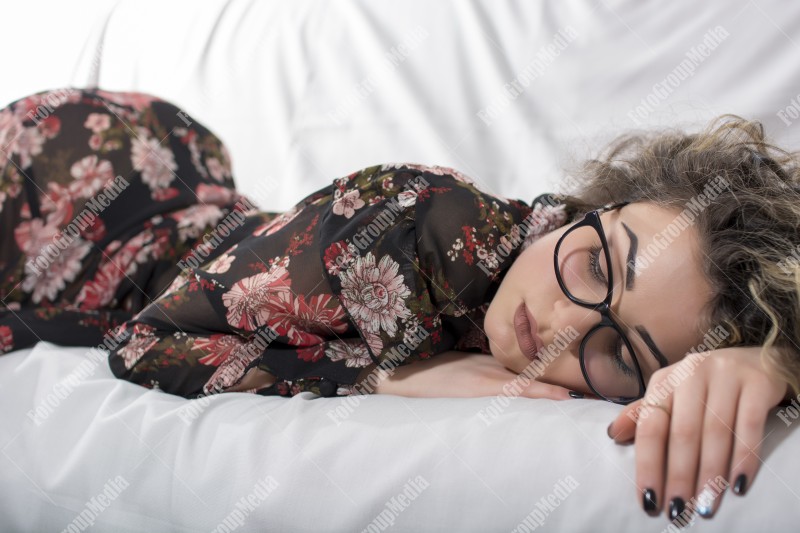 Woman with curly hair and floral dress posing on bed