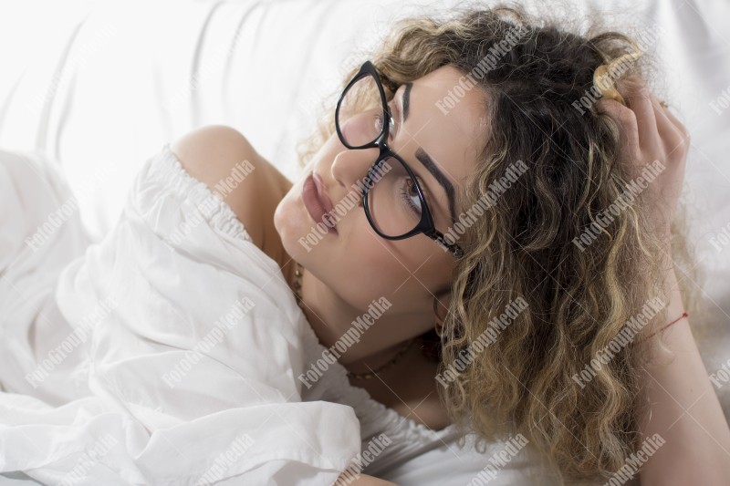 Woman with curly hair and white dress posing on bed