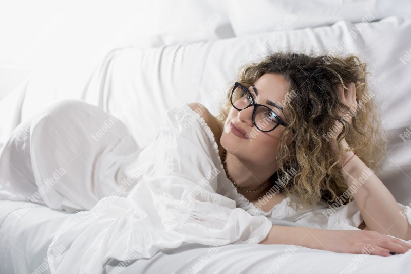 Woman with curly hair and white dress posing on bed