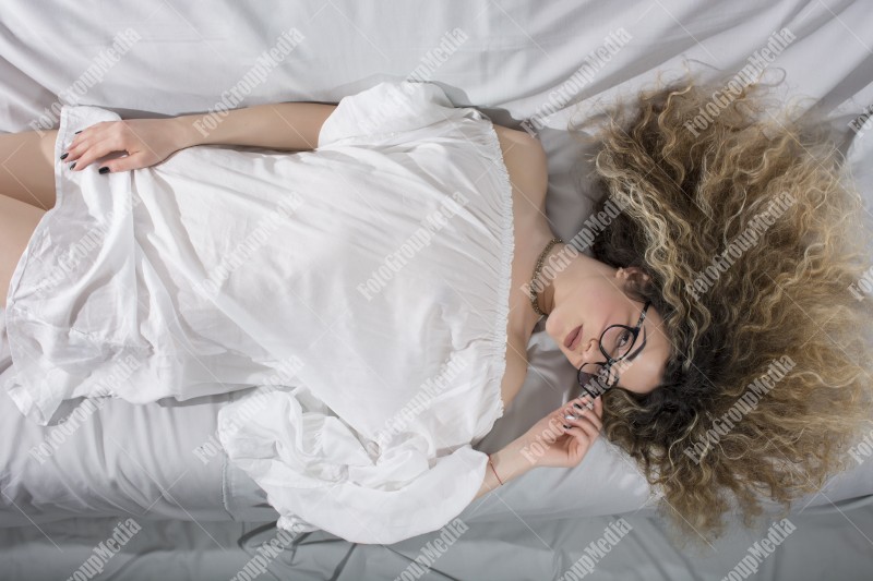 Woman with curly hair and white dress posing on bed