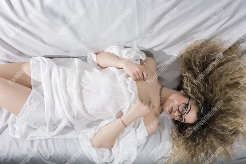 Woman with curly hair and white dress posing on bed