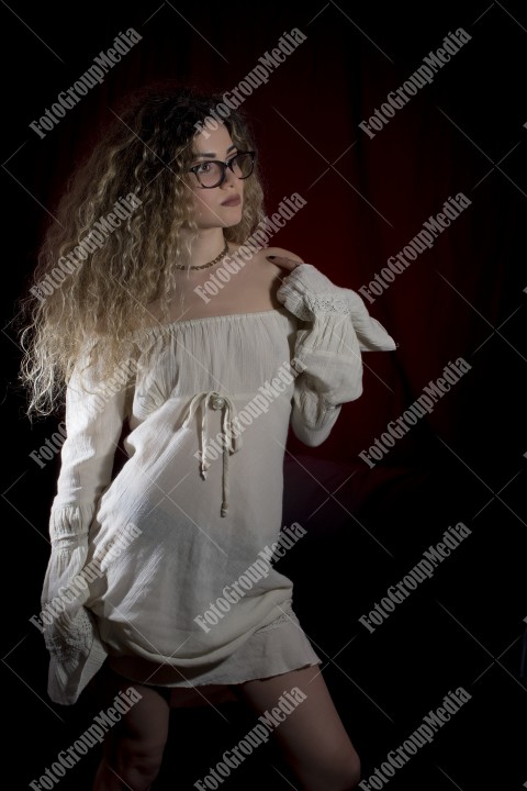 Woman with curly hair and white dress posing on black background