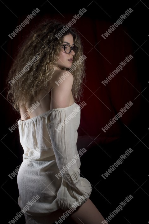 Woman with curly hair and white dress posing on black background