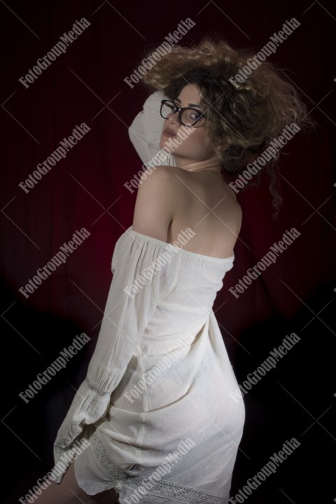 Woman with curly hair and white dress posing on black and red background