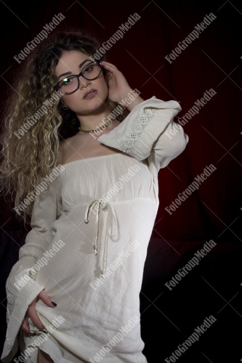 Woman with curly hair and white dress posing on black and red background