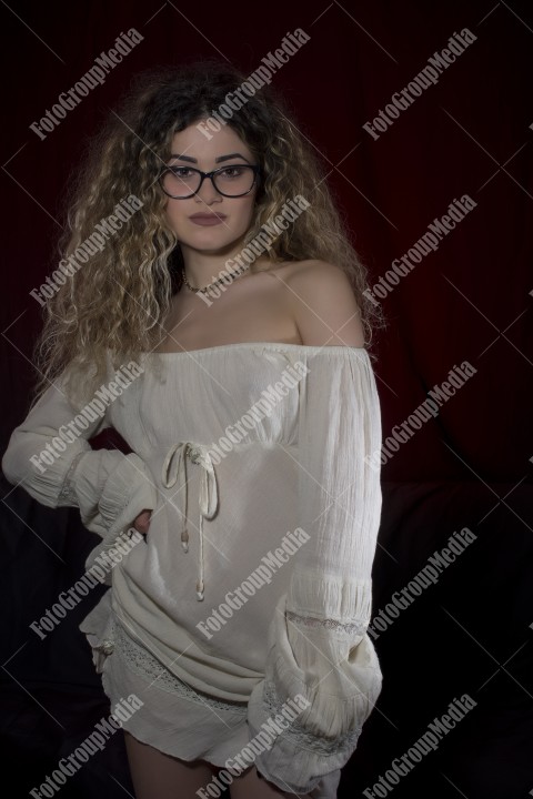Woman with curly hair and white dress posing on black and red background