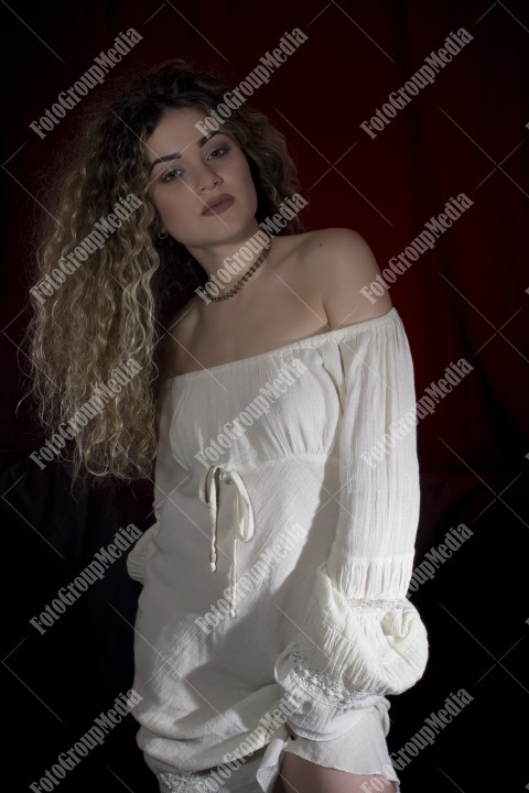 Woman with curly hair and white dress posing on black and red background