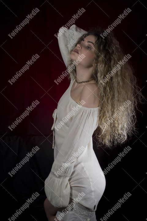 Woman with curly hair and white dress posing on black and red background