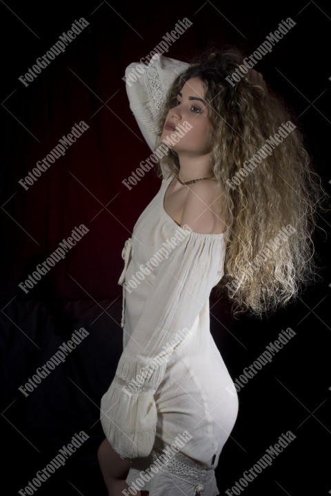Woman with curly hair and white dress posing on black and red background
