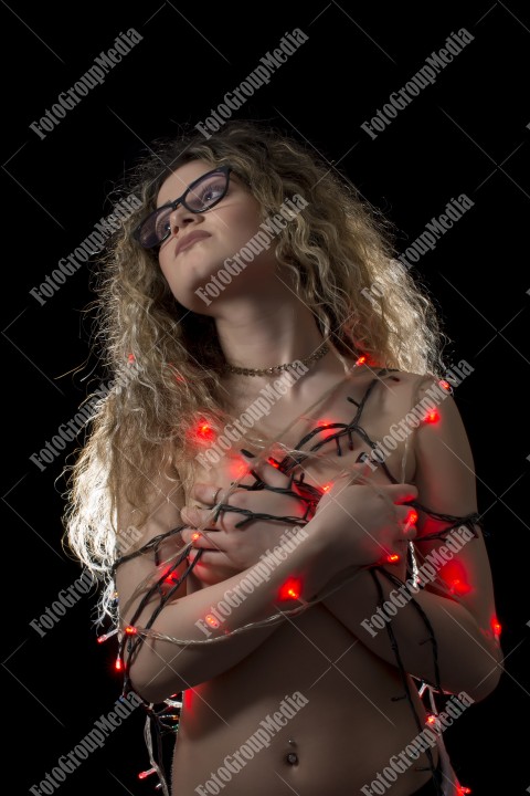 Woman with curly hair wrapped in Christmas lights posing on black background