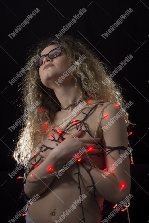 Woman with curly hair wrapped in Christmas lights posing on black background