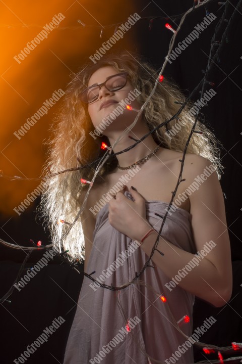 Woman with curly hair wrapped in Christmas lights posing on black background