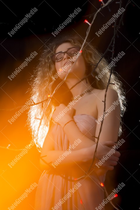 Woman with curly hair wrapped in Christmas lights posing on black background