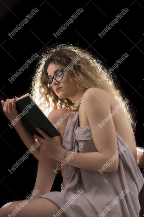 Woman with curly hair and eyeglasses reading a book sitting on chair