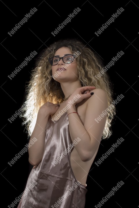 Woman with curly hair and satin lingerie posing on black background