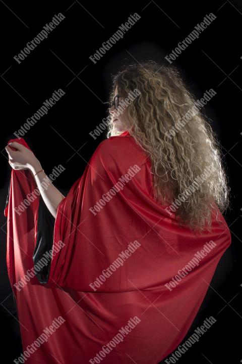 Woman with curly hair dressed in red panties and red cape posing on black background