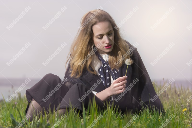 Young girl sitting on grass and playing with dandelion