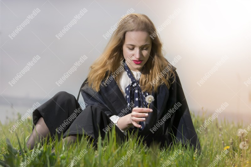 Young girl sitting on grass and playing with dandelion